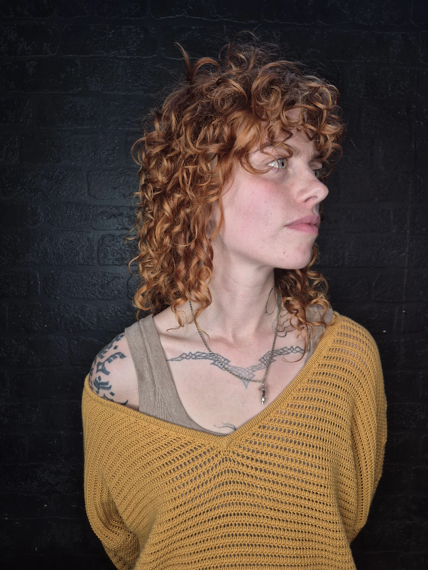 Copper curly hair against a dark brick wall